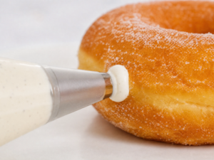 Piping vanilla whipped cream into a golden fried doughnut